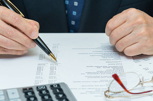 Man reviewing financial reports Financial reports being reviewed by an executive. The business man in a blue suit is cheking the document with a ballpoint pen in the hand. There are a calculator and glasses on the desk. (XXXLarge) cfo stock pictures, royalty-free photos & images