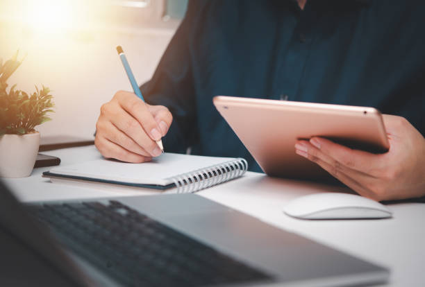 istock Man Hands Writing Goals, Plans, and Wish List on Notebook in Office Creativity and Learning and To-Do List on Desk in Educational Motivation Work Office Environment. 1573525782
