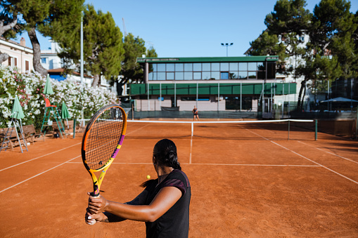 Tennis player in black outfit practicing during a training with her coach in daylight under a harsh sun.