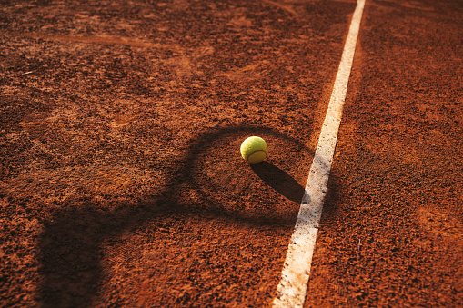 High angle view of a tennis racket on a clay court near baseline.