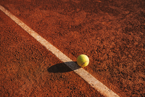 Tennis ball hitting baseline on clay court.