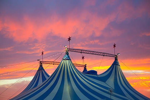 Top of blue and white circus tent against a vivid sunset Circus tent in a dramatic sunset sky colorful orange blue with lights circus photos stock pictures, royalty-free photos & images