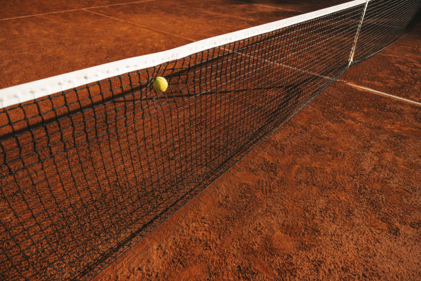 Tennis ball hitting the net during a tournament match on clay court.