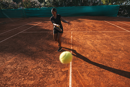 Young woman in black outfit training on clay soil court.