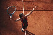 Professional tennis player serves on clay court