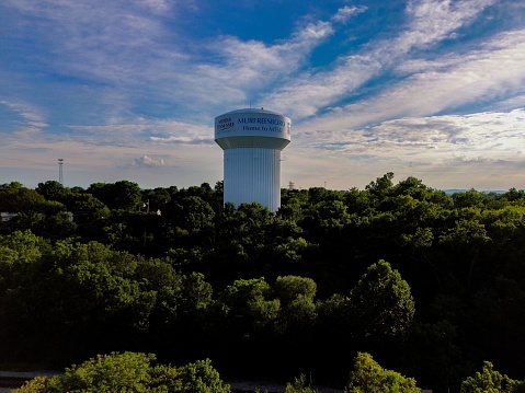 Murfreesboro, United States – July 11, 2023: A cylindrical concrete water tower surrounded by lush green trees at sunset in Murfreesboro