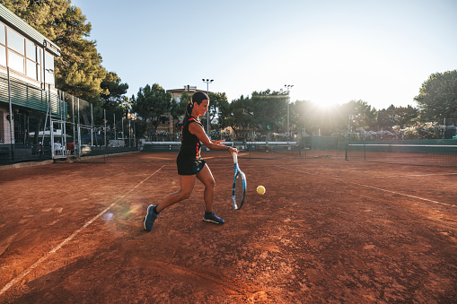 Black outfit professional tennis player training on clay court under the sun.