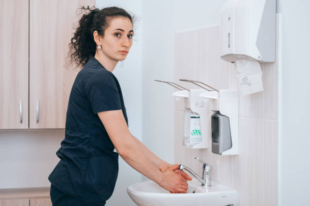 une jeune infirmière adulte concentrée qui se lave les mains au cabinet médical se prépare à l’examen médical du patient. une jeune femme médecin espagnole bouclée fatiguée de se laver les mains après l’opération. médecine, soins de santé. - clothing professional occupation medical occupation doctor photos et images de collection