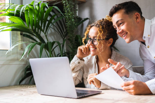 istock Two people working together with computer at the desk in home office workplace. One young man and adult woman smile and enjoy small business. Entrepreneur with assistant using computer wireless online 1573588259