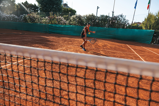 Young woman in black outfit training on clay soil court.