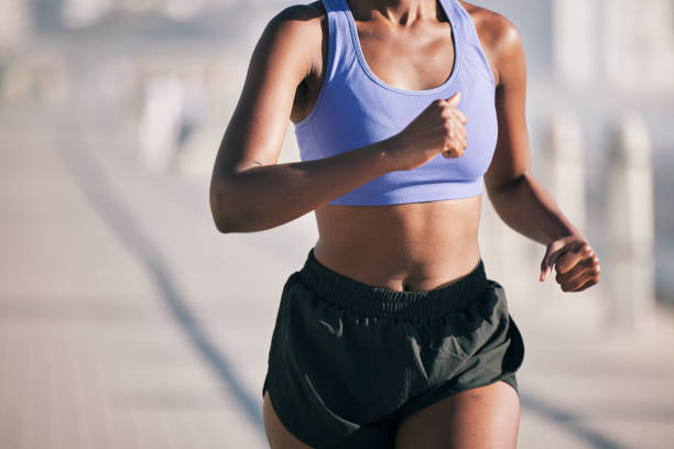 primo piano, donna e corpo che corrono all'aperto al sole per la maratona, le prestazioni sportive e il fitness. corridore femminile, allenamento cardio e sano allenamento estivo per energia, azione veloce ed esercizio urbano - endurance sport foto e immagini stock