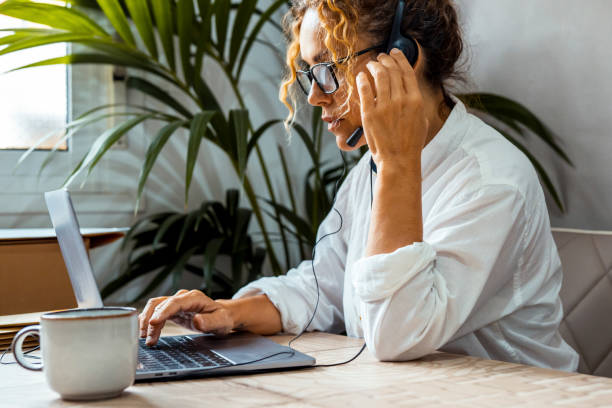 istock One woman worker alone using computer and headset to made video voice call at the desk in small business home office leisure activity. Professional female freelance at work. Laptop job people indoor 1573590534