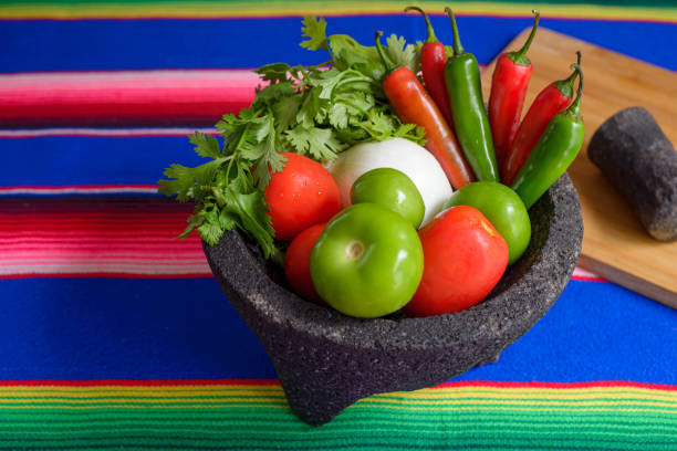 istock Molcajete with vegetables on a colorful serape. Ingredients for a hot sauce. 1573603356