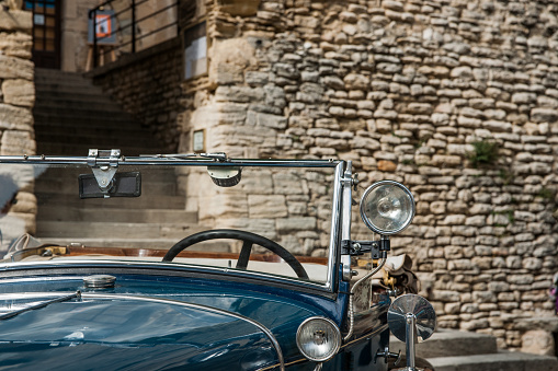 Gordes, France - MAy 1 2011; Vintage blue car windscreen and lights in close-up parked in front historic stone building in picturesque French hilltop walled town.