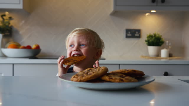 Mischievous Young Boy Taking Giant Cookie From Plate In Kitchen At Home