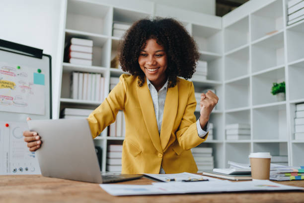 istock American African business woman using document, computer laptop, calculator, paperwork, documents, in winner and smiling Happy to be successful achievement success. finance and investment concepts 1573630836