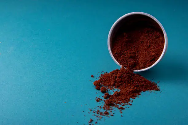 Aluminium filter with brown coffee beans on a teal blue surface with ground beans.