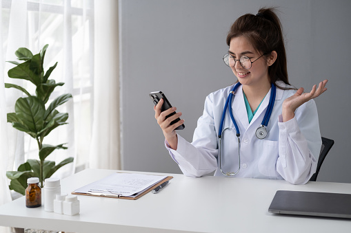 Female Young Asian doctor making video call with patient by smartphone cell phone laptop tablet