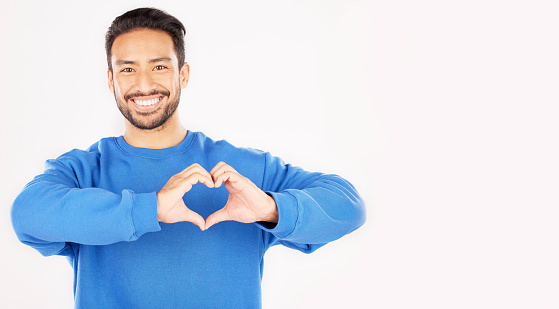 Portrait, heart and hands of man in studio, white background and care for kindness on mockup space. Happy asian male model with finger shape for love icon, thank you and emoji in support of freedom