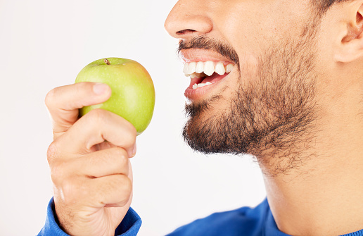 Closeup, man and hands with apple for diet, natural nutrition or vitamin against a white studio background. Mouth of male person eating healthy organic fruit or bite for wellness, detox or fiber