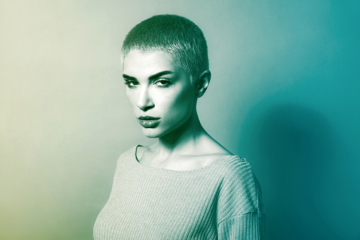 Black and white of young rebellious female model with short blond hair and makeup in knitted sweater looking at camera with confidence in studio
