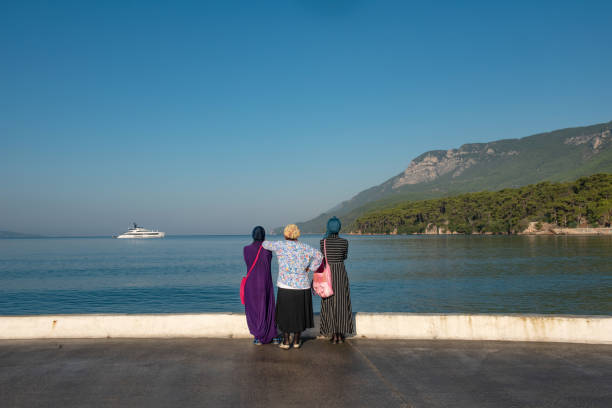 Muslim women visitors to the Turkish seaside town of Akyaka admire the beautiful view and expensive yacht moored in the bay. Turkish coast, Mugla.