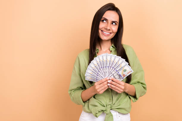 Portrait of cheerful positive woman long hairdo wear green shirt hold money look at casino empty space isolated on beige color background stock photo