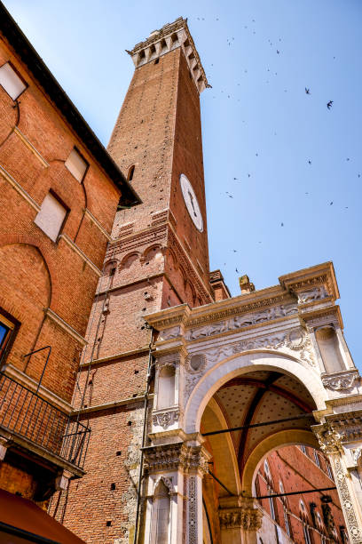 The Cappella di Piazza and the Torre del Mangia in Piazza de Campo in the medieval heart of Siena A suggestive view from below of the Cappella di Piazza (Chapel of the Square) on the facade of the Palazzo Pubblico in Piazza del Campo, in the medieval heart of Siena, in Tuscany. Located on the left side of the palace under the Torre del Mangia, this chapel is a marble tabernacle in Gothic style built in 1352 in honor of the Virgin Mary for having saved the city from the plague of 1348. Built in 1290 as the seat of the Council of Nine and of the executive power of the medieval city, the majestic Palazzo Pubblico is still the seat of the municipal government of Siena. The Torre del Mangia was built between 1338 and 1348 on a project by Giovanni Balduccio, known as the 'Mangia', becoming the symbol of the political and military power of Siena compared to its rival Florence. Center of the city life since 1169, Piazza del Campo or simply Campo is one of the most beautiful and famous squares in the world for its particular shell shape. In this space every year the seventeen historical districts of Siena compete in the Palio, one of the oldest horse races in the world. Siena is one of the most beautiful Italian cities of art, in the heart of the Tuscan hills, visited for its immense artistic and historical heritage and for its famous popular traditions. Since 1995 the historic center of Siena has been declared a World Heritage Site by UNESCO. Image in high definition quality. torre del mangia stock pictures, royalty-free photos & images