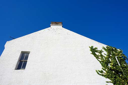 Close-up on a side wall of a building with vines, a window, chimney, and deep blue sky beyond.