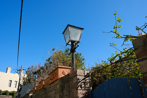 Antique black street lamp on a wall against a blue sky.