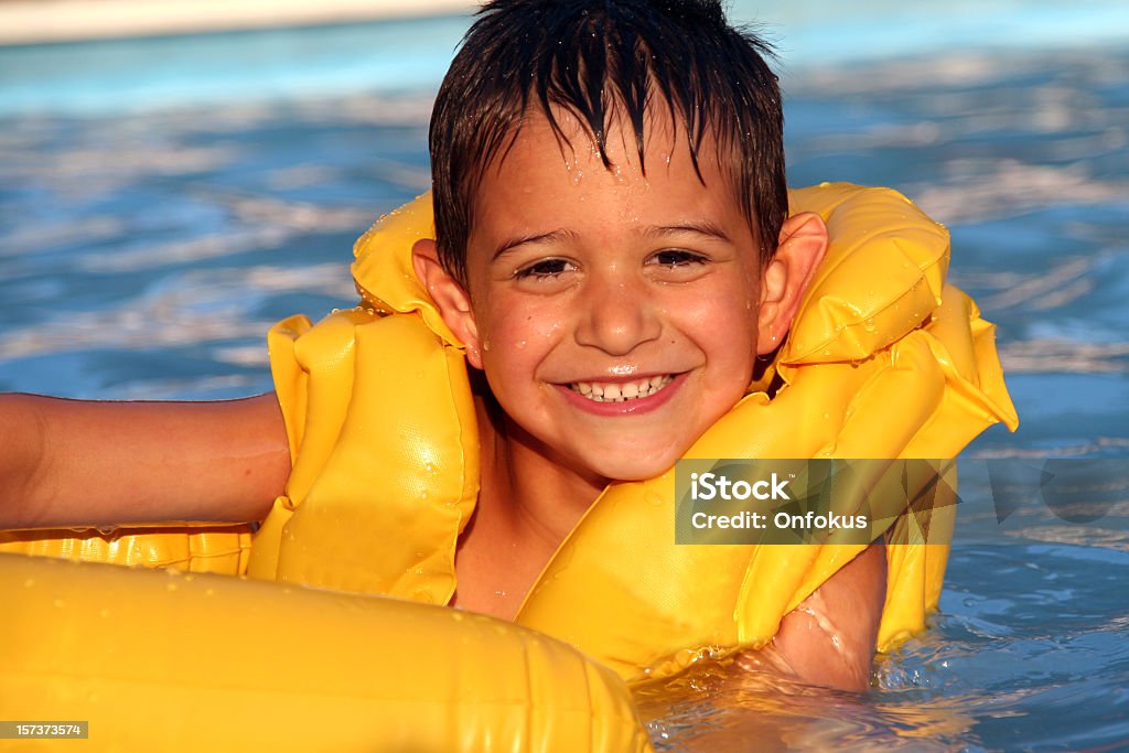 Child Wearing a Yellow Life Jacket in Swimming Pool DSLR picture of a Child in swimming pool. The young boy is wearing a yellow life jacket and is having fun in the water. The boy have a big smile and the natural light is from the sun on a nice summer day. Baby - Human Age Stock Photo