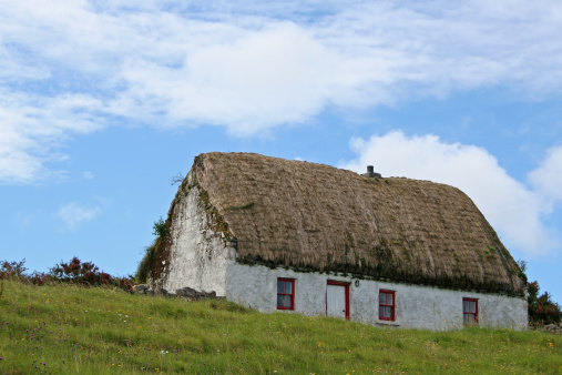 Classical thatched cottage with green grass upon a blue sky. The photo was taken in Inis Mor