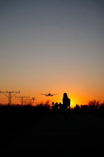 A backlit woman looks at a plane at sunset as a sign of nostalgia and memories.