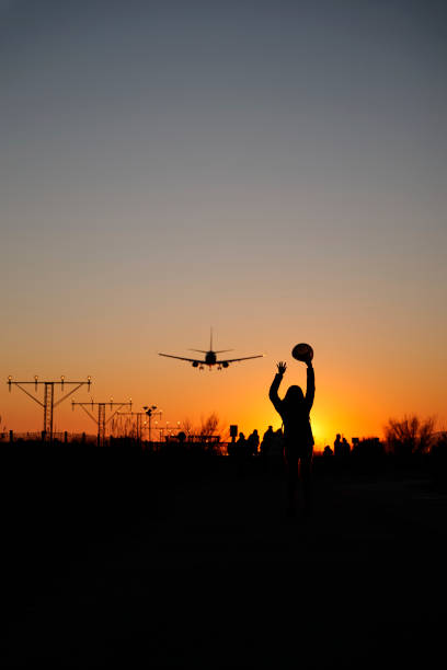 A backlit woman raises her arms to airplanes at sunset as a sign of travel and adventure.
