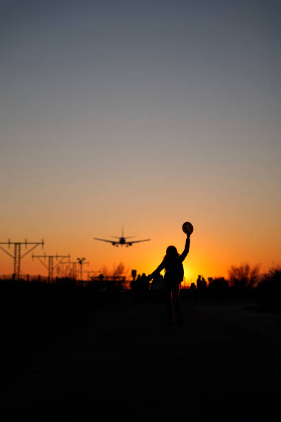 A backlit woman raises her arms to airplanes at sunset as a sign of travel and adventure.
