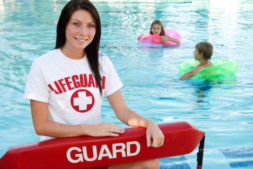 Female lifeguard next to swimming pool.
