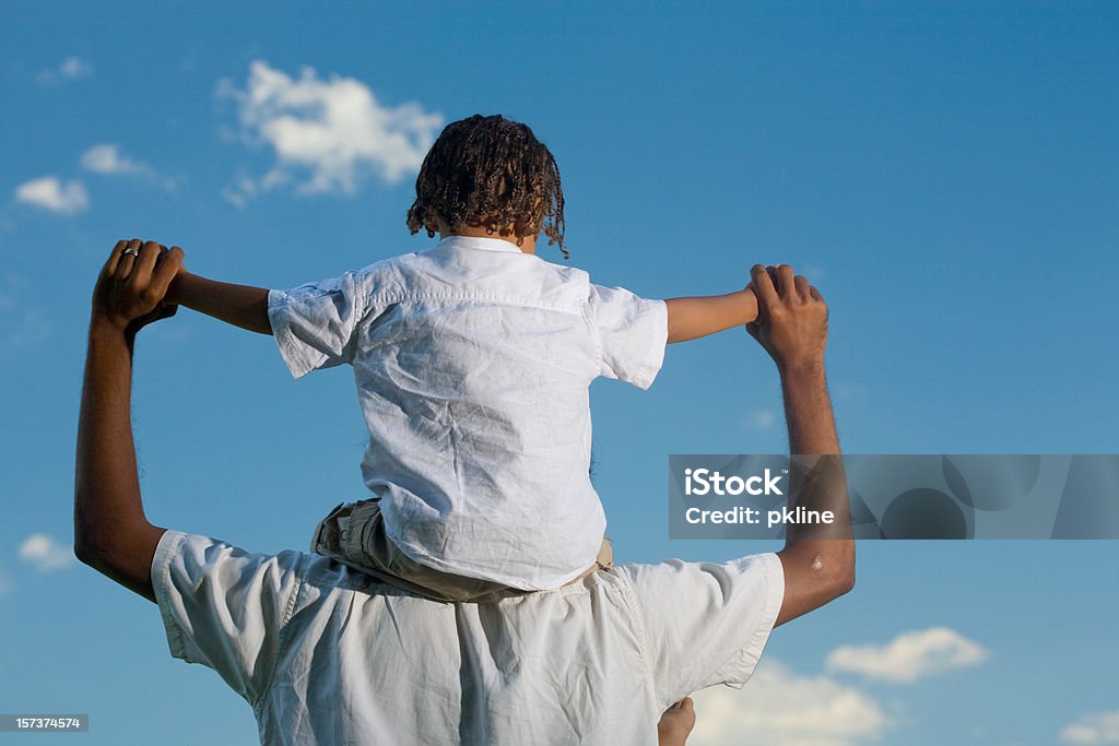 Vista traseira de um menino nos ombros do pai sob o céu azul - Foto de stock de Criança royalty-free