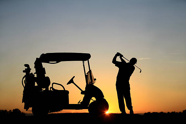 Caucasian Male Senior Golfer with Golf Cart at Sunset A silhouette of a senior male Caucasian golfer at sunset with powercart. Golfer is demonstrating great form and balance as he swings into a finish position. Image can be used for teaching, golf academy, lessons, senior, retirement, golf resort, golf vacation, back view, athlete, leisure, sports, weekend activities, unrecognizable people, swinging, instruction, and golf cart communities.  night golf stock pictures, royalty-free photos & images