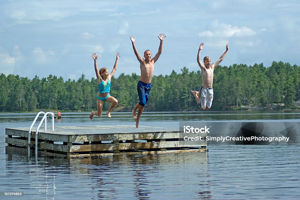 Siblings Jumping into Lake Teenage siblings jump with excitement into a lake on their summer vacation. Cottage Stock Photo