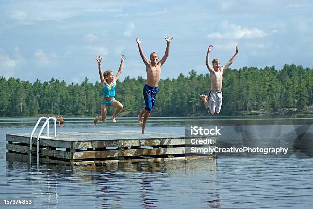Siblings Jumping Into Lake Stock Photo - Download Image Now - Cottage, Pier, Lake