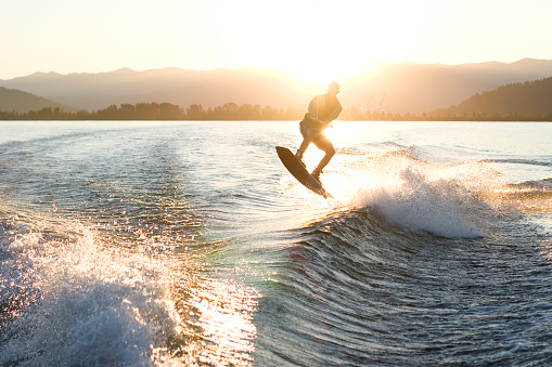 Athletic young man wake surfing on a wave in the lake, spinning mid-air doing a trick.