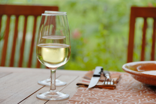 2 glasses of white wine at a table, in a patio on a wonderful summer evening, garden in background