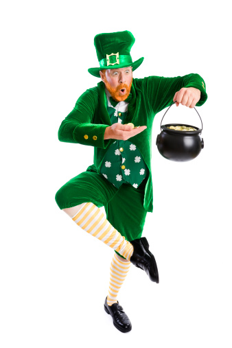 Full length leprechaun get excited and dances a jig with his pot of gold coins; copy space 