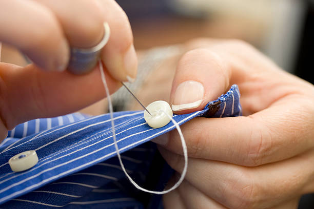 Close-up of a person sewing on white button on striped shirt stock photo