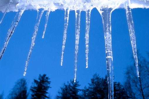 Icicles hanging from the gutter, with trees and blue sky in the background.