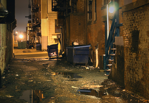 Dark gritty inner city urban alleyway. Photo of a seedy, dirty, and dangerous looking  alley at night 