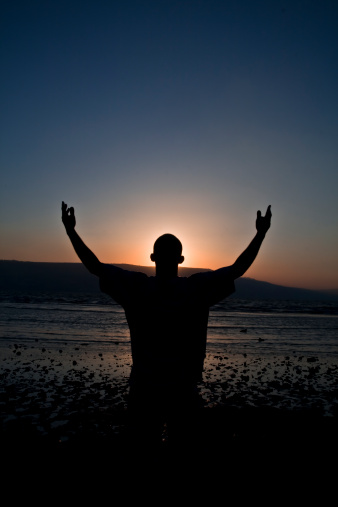 A man stands in admiration and praise on the edge of the sea of Galilee with his arms raised in the air.(a.k.a. the Kinneret or Lake Tiberius), Israel.  Vertical with copy space.