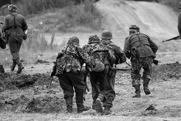 WW2 Attacking Troops. German era WW2 re-enactors advance towards the enemy.Major re-enactment battle at the War and Peace show.Picture has been aged to give the feel of a vintage photo. battle reenactment stock pictures, royalty-free photos & images