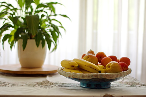 Bowl with fruits and potted plant on table against curtain