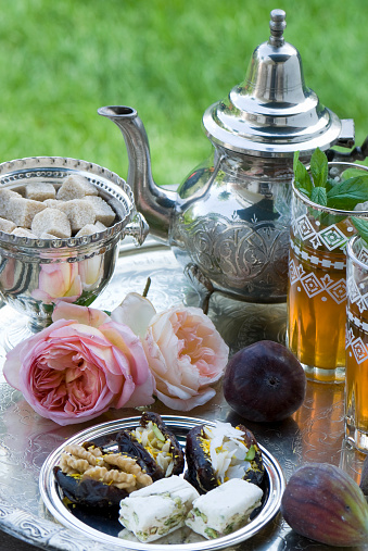 A set of old silverware, Moroccan tea glasses with tea and mint, some figs and some Moroccan sweets lovingly decorated with some roses.